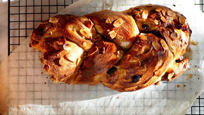 Birds eye view of a braided bed loaf with sultanas and almond on top, on a paper-lined backing tray.