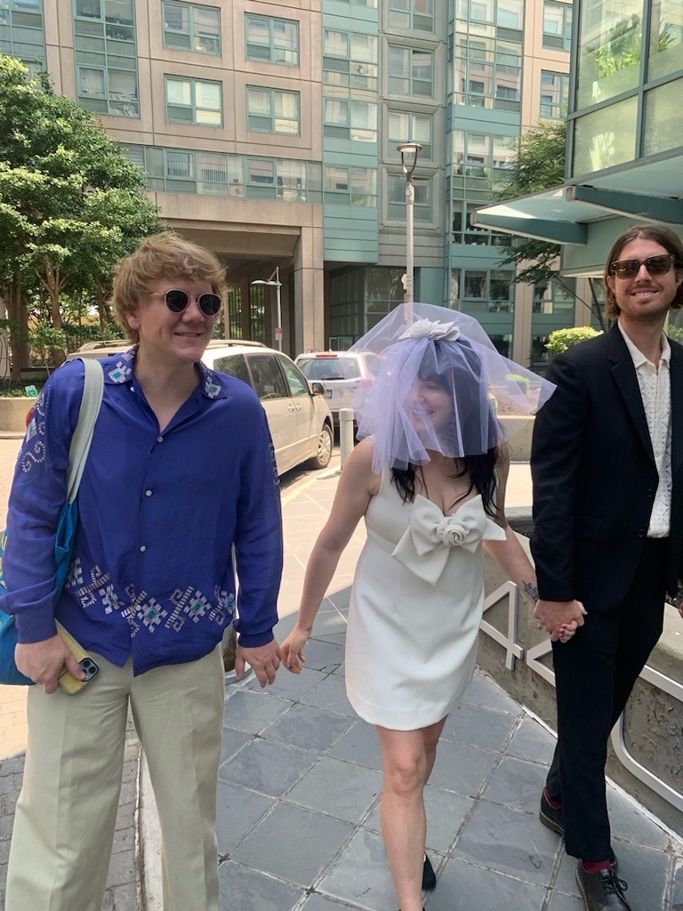 Josh Thomas, left, walks next to Emily Barclay in a wedding dress and veil, centre, with Tom Ward, right.