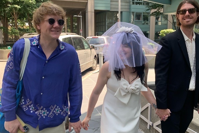Josh Thomas, left, walks next to Emily Barclay in a wedding dress and veil, centre, with Tom Ward, right.