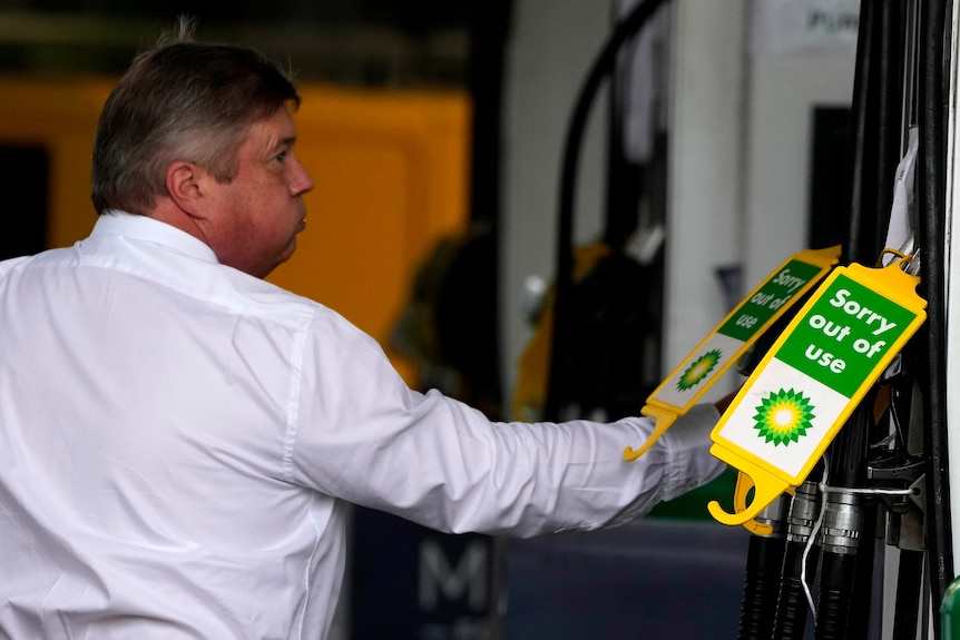 A man in a white shirt looks at fuel bowsers which have a 'sorry out of use' sign on them.