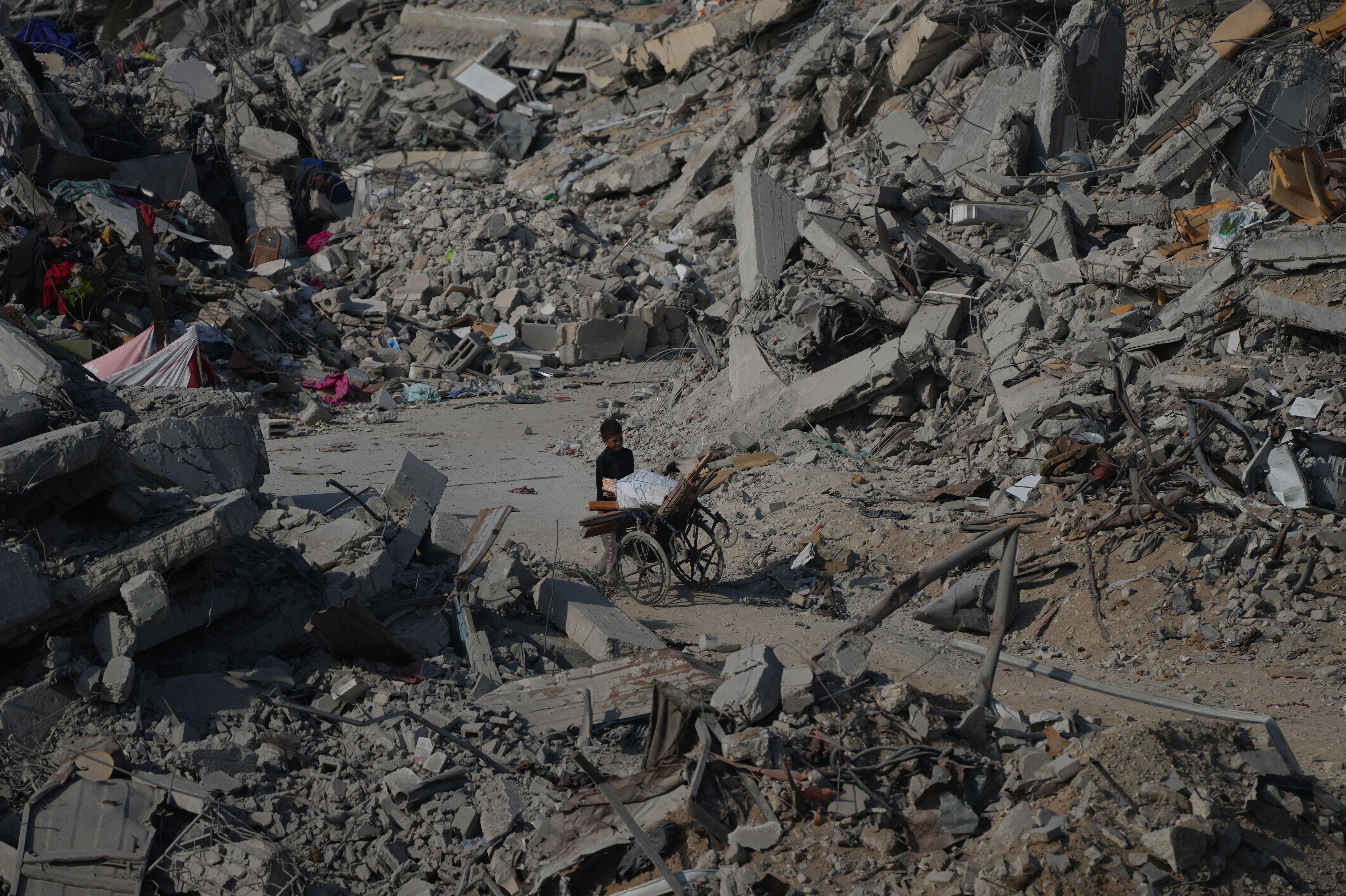 A boy pushes a wheelchair through the rubble.