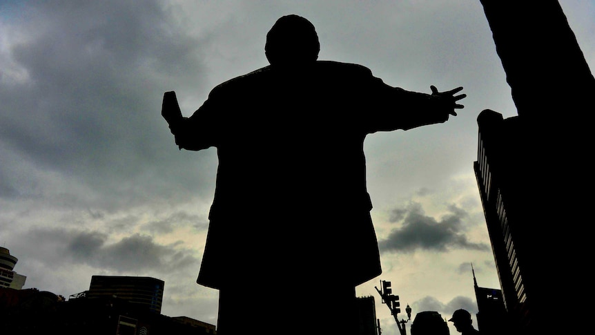 back shadow of figure hold a bible in one hand and the other outstretched in street setting