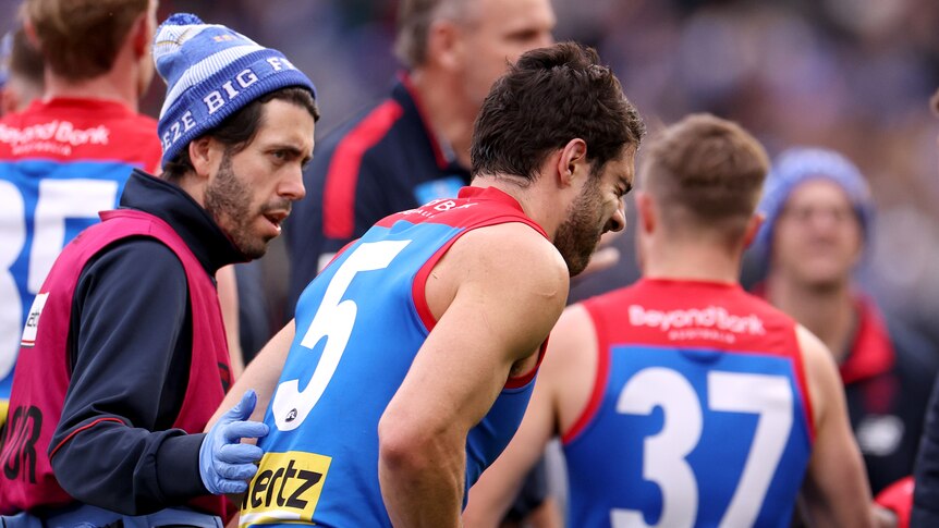 Melbourne Demons' Christian Petracca walks off the field in the hands of a trainer during an AFL game.