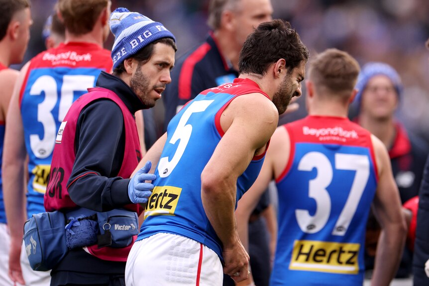 Melbourne Demons' Christian Petracca walks off the field in the hands of a trainer during an AFL game.