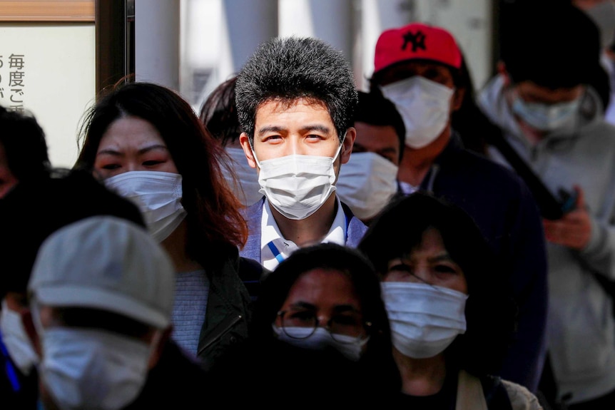 A group of people walking through a Tokyo train station wearing face masks.