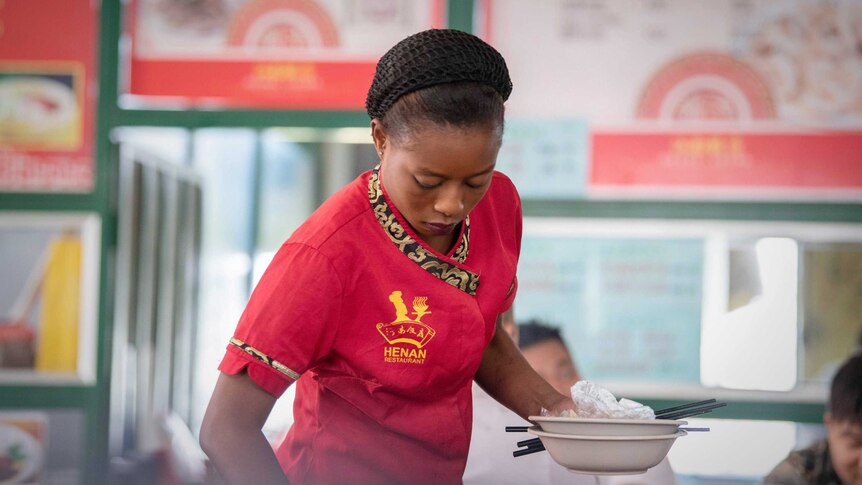 A Zambian waitress clears plates at a food hall comprising Chinese eateries and shops.