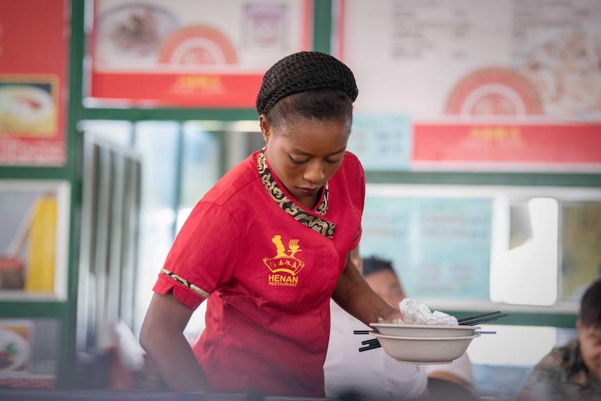 A Zambian waitress clears plates at a food hall comprising Chinese eateries and shops.