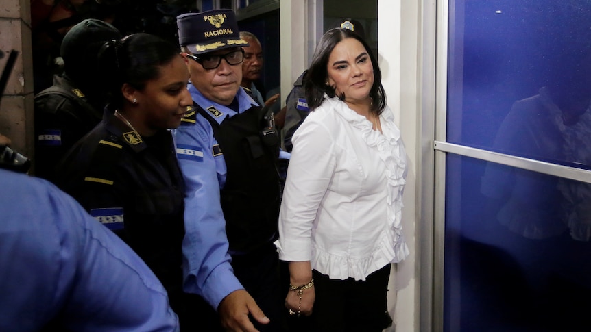 A woman smiles as police escort her through a doorway. 
