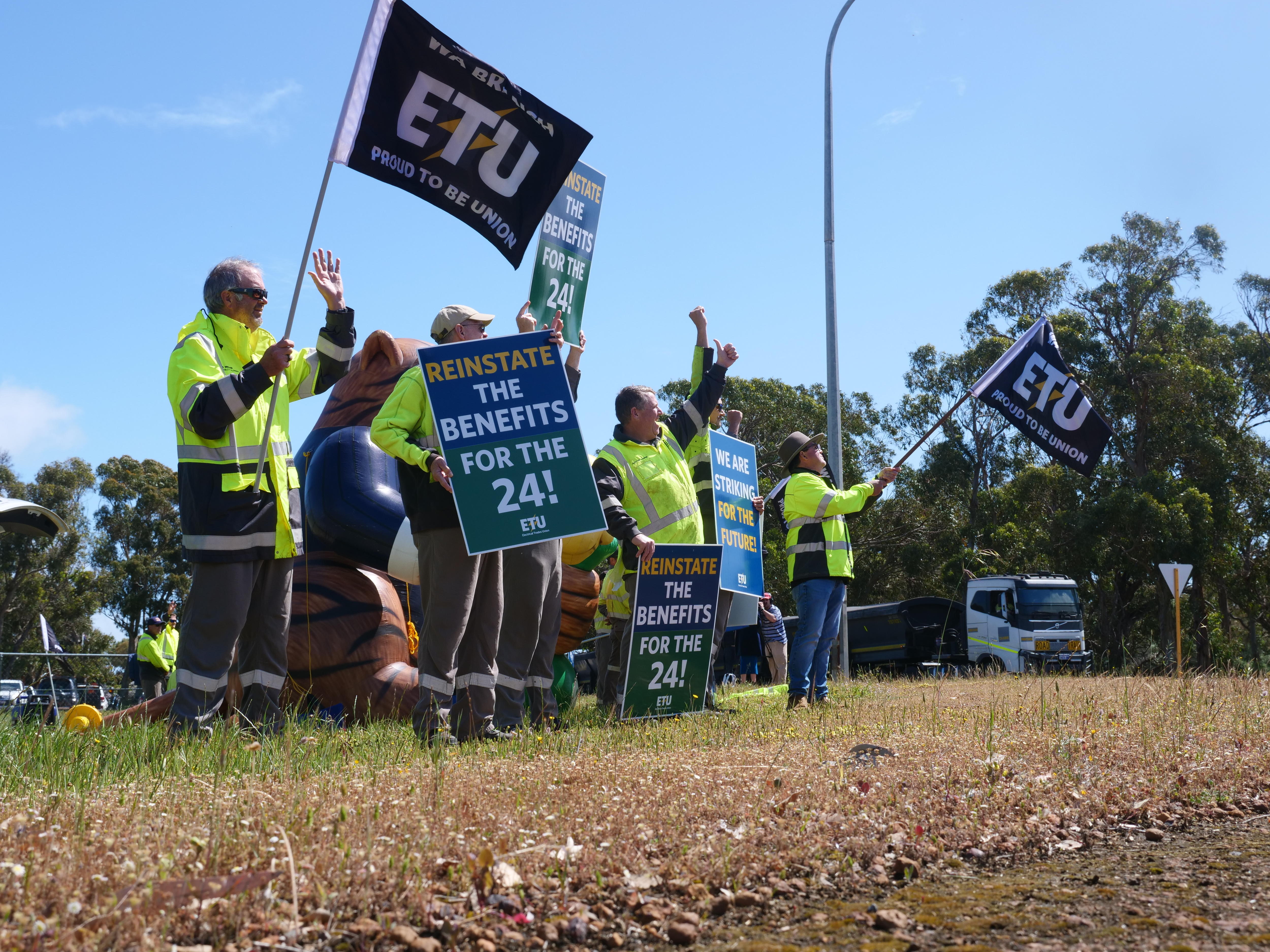 A group of men wearing high-visibility clothes and carrying protest and union signs during a strike.