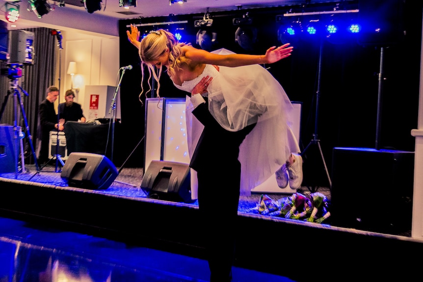 A boy wearing a suit holds a girl wearing a white dress up in the air.