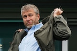 Roman Abramovich, a man with grey hair and stubble, shrugs a khaki jacket on over his blue shirt