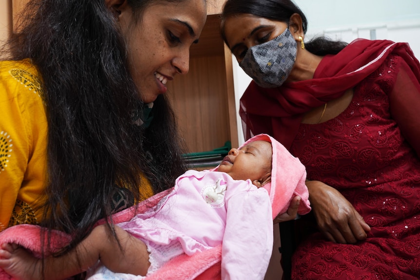 Mother holds baby in her arms, while the child's grandmother looks on. 