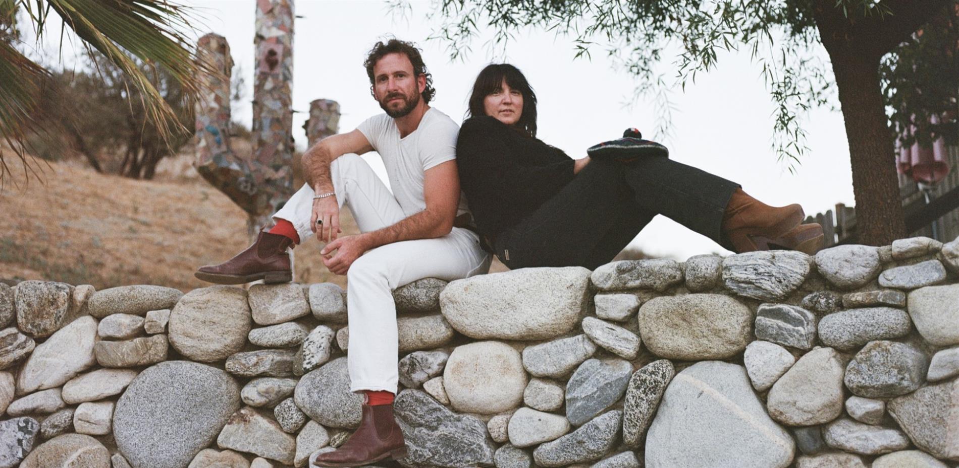 Two people sitting on a stone wall, a man and woman in the daytime
