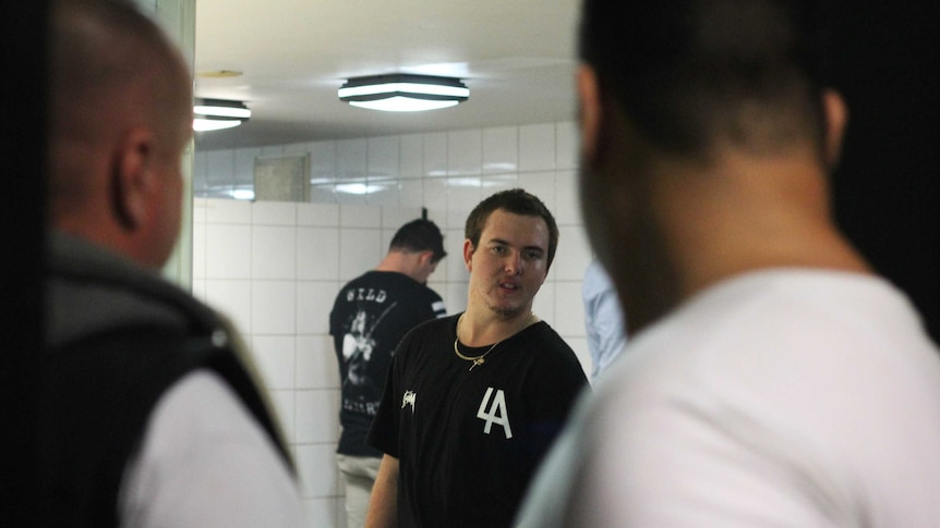 A man in a bathroom looks at two men who are looking at him.