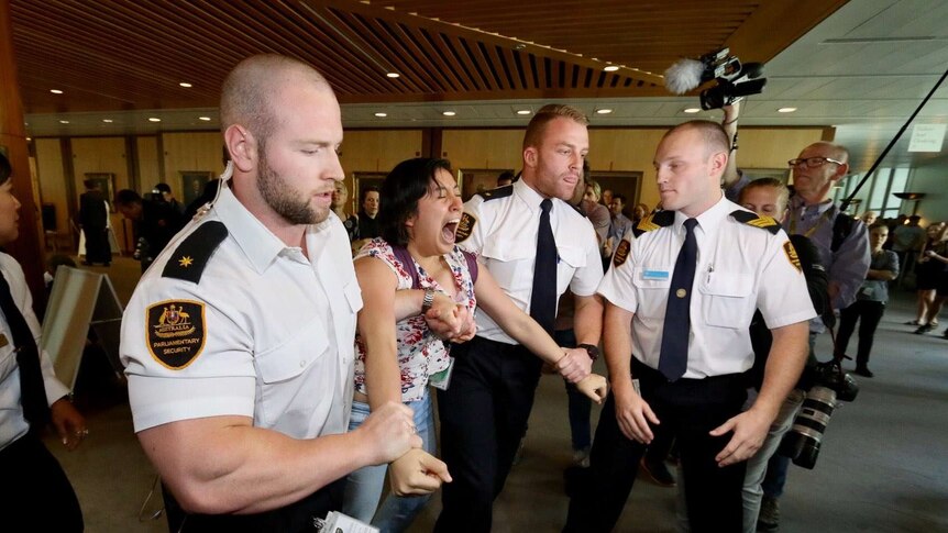 A woman shouts as she is dragged out of Question Time by Parliament House security guards.