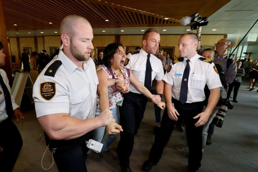 A woman shouts as she is dragged out of Question Time by Parliament House security guards.