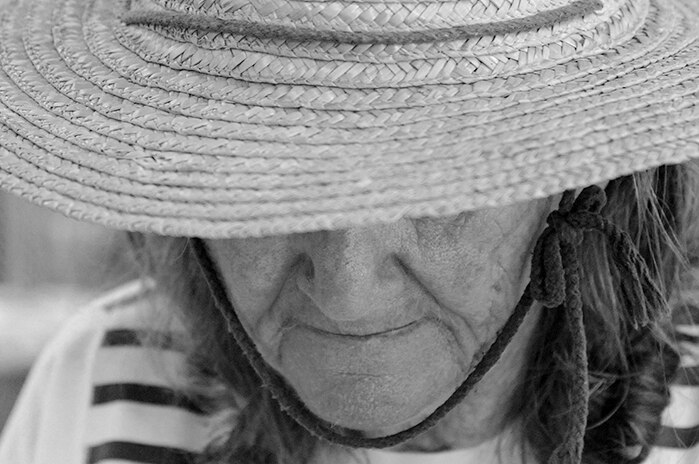 A close-up black and white photo of a woman wearing a straw hat, with her eyes shielded by its brim.