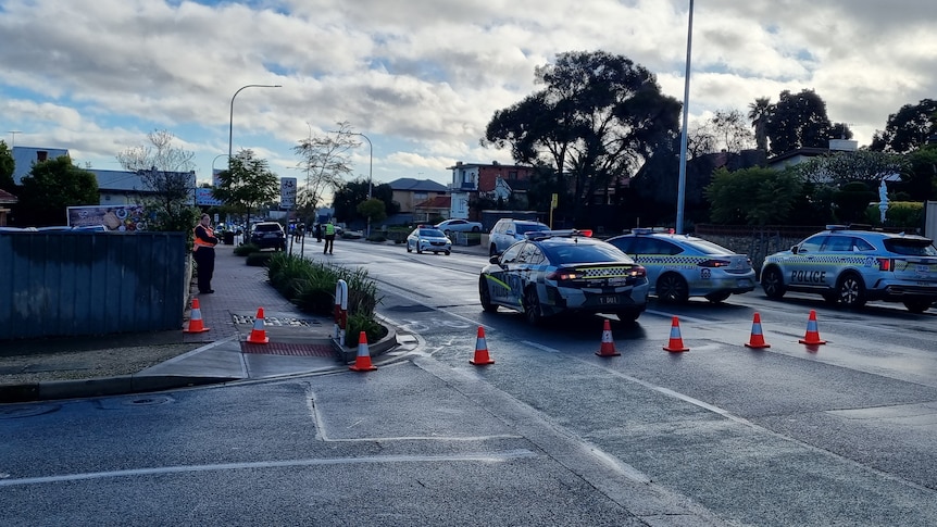 Police cars parked across a road with witch's hats on a wintry day