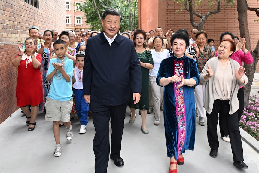 Xi Jinping walks, surrounded by people clapping.