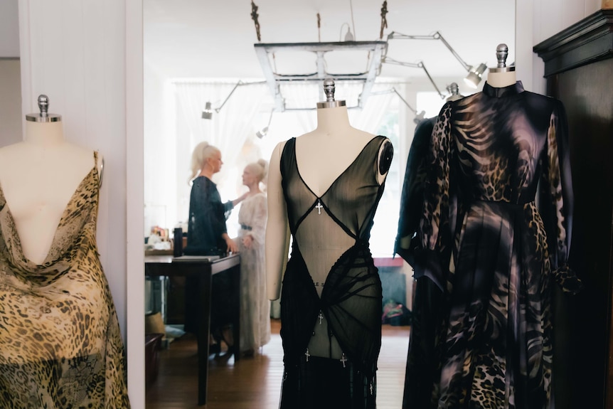 Three mannequins with sheer dresses draped over them stand in an atelier showroom.