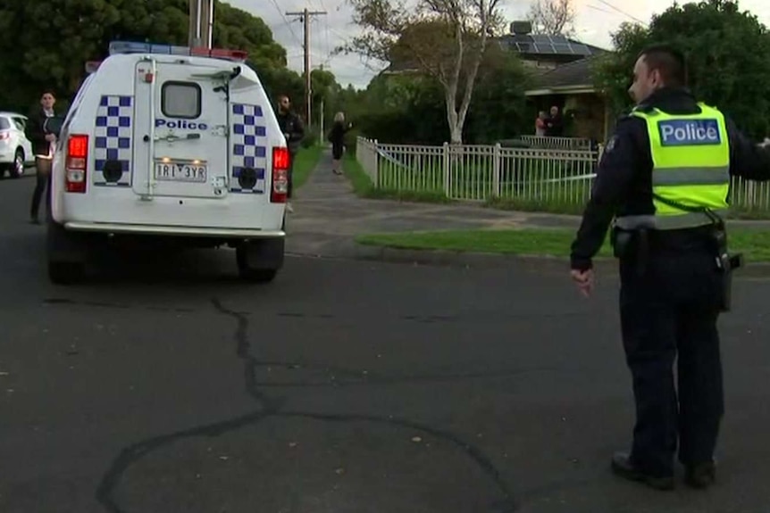 A suburban street with a police car and a police officer holding police tape.