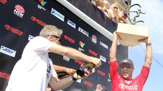 Newcastle MP Tim Owen showers 2013 Surfest winner Joel Parkinson with sparkling wine, as he holds up the Mark Richards Trophy.