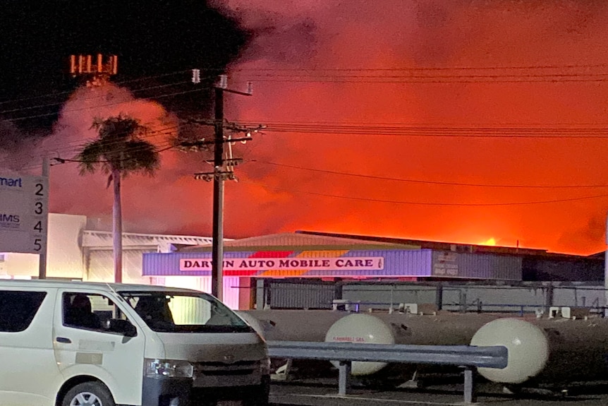 Fire soars into the sky above an industrial business during the night.