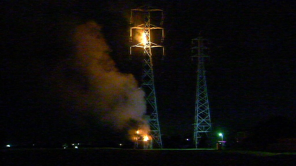 Two fires burn on a mobile phone tower, one near the base and the other near the top.