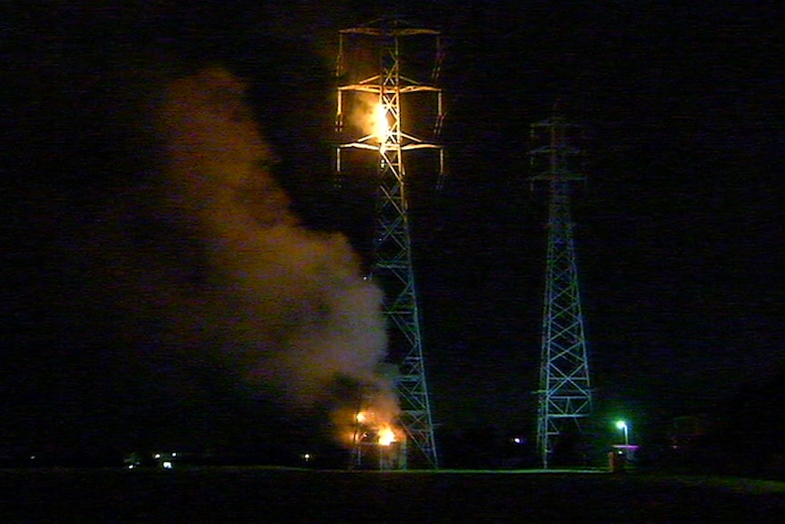 Two fires burn on a mobile phone tower, one near the base and the other near the top.