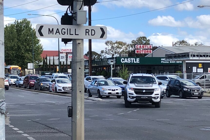 Signage for Magill Road with traffic driving across the intersection in the background