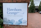 A white sign with the name Hawthorn Grange in blue font in front of a brick carpark.