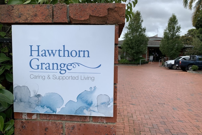 A white sign with the name Hawthorn Grange in blue font in front of a brick carpark.