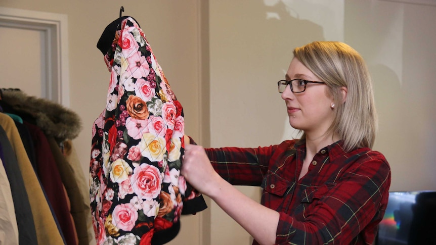 Blonde lady holds up a rose patterned jacket off the clothes rack.