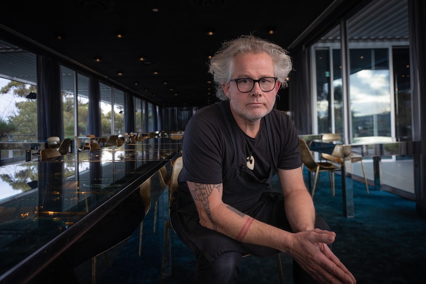 A man with silver hair sits on a chair in a restaurant