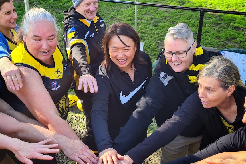 Sarah Loh and other team players place their hands in together on a football field.