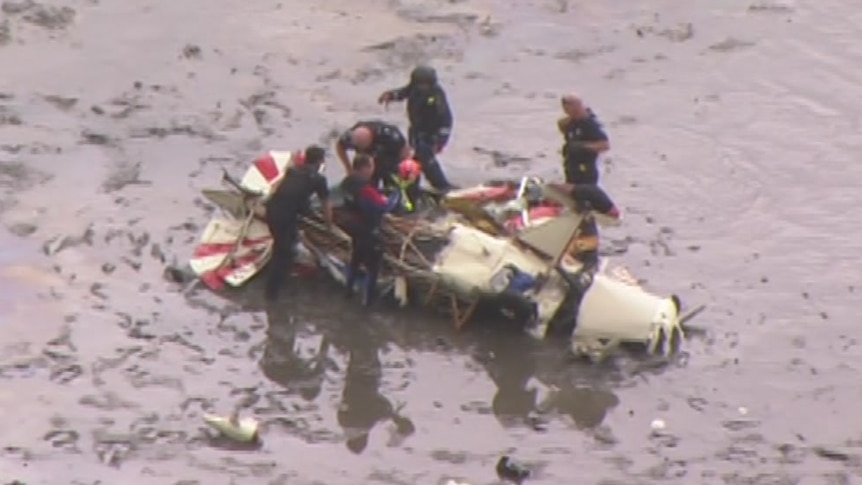 Rescue workers stand over the wreckage of a light plane.