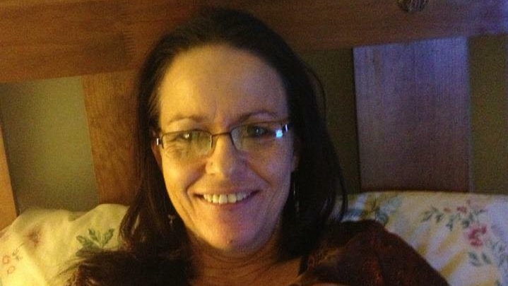 A woman sits in bed, smiling at the camera.