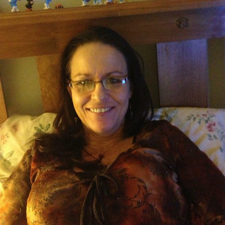 A woman sits in bed, smiling at the camera.