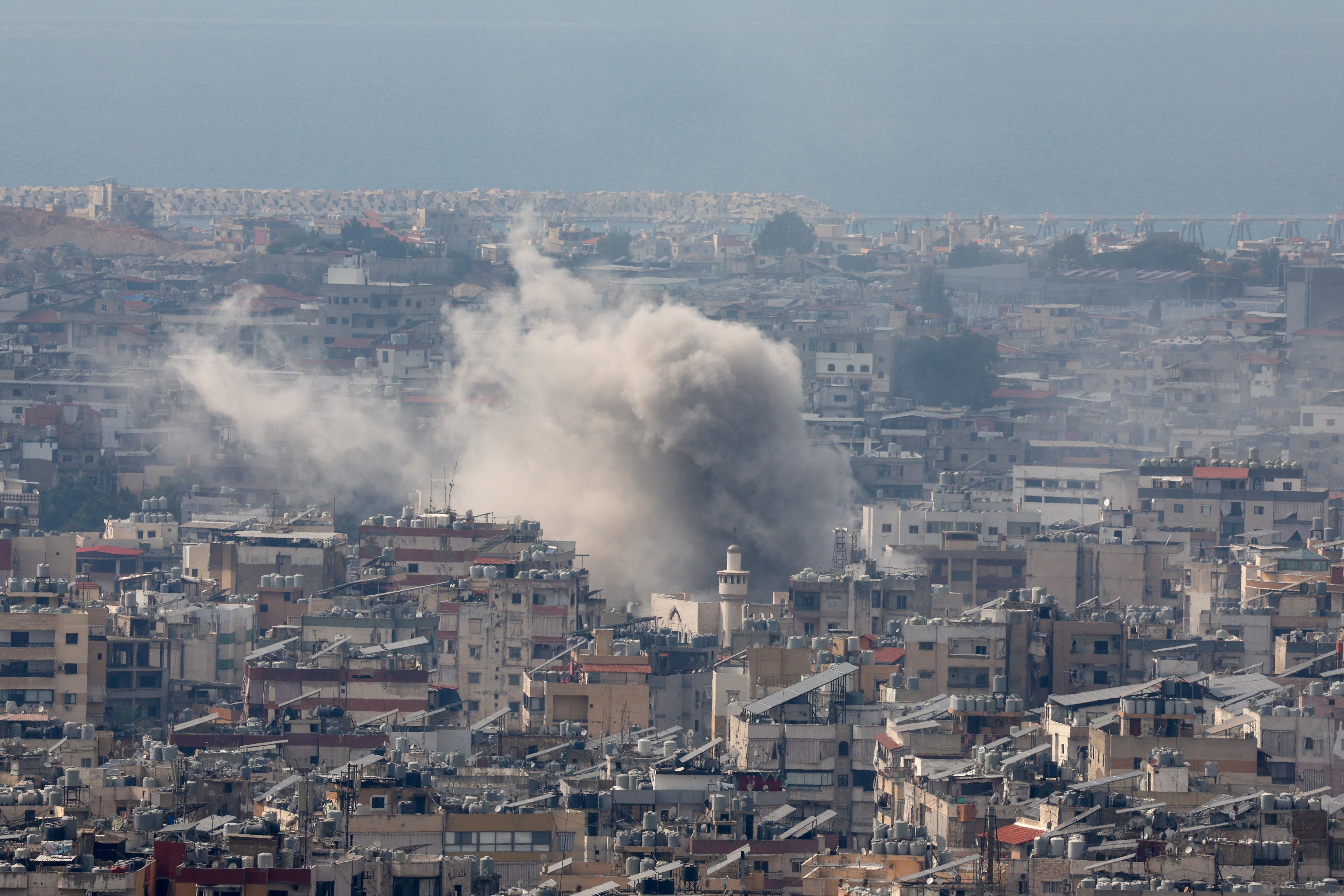 A large cloud of grey smoke rises from a sprawling city suburb of apartment blocks