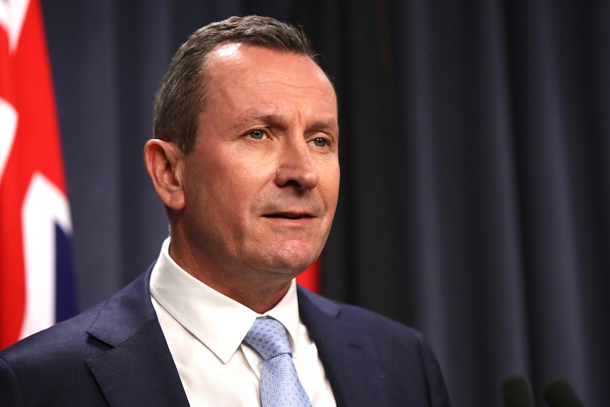 Mark McGowan in a suit and light blue tie standing at a lectern in front of an Australian flag.