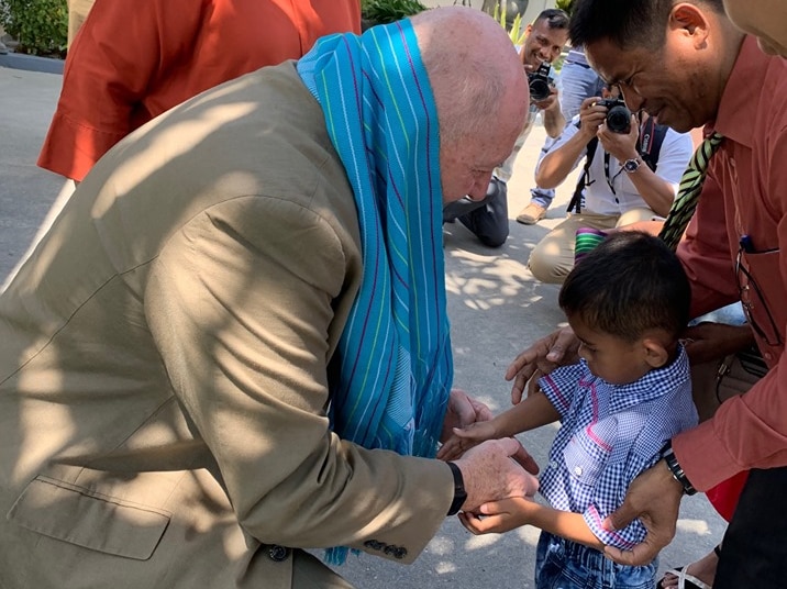 Peter Cosgrove crouches down to shakes hands with shy-looking boy, while his family watch on smiling.
