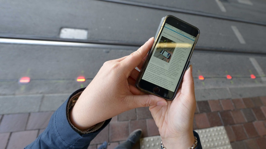 A line of lights embedded in the pavement can be seen past a hand using a mobile phone.