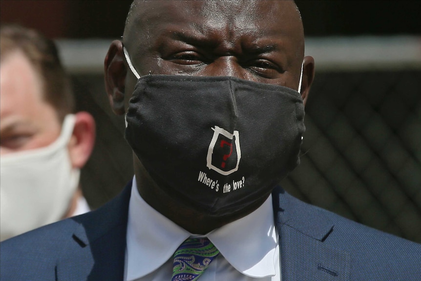 A headshot of a black man wearing a suit and a face mask