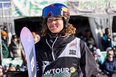 Valentino Guseli carrying his snowboard and smiling after a competition. 