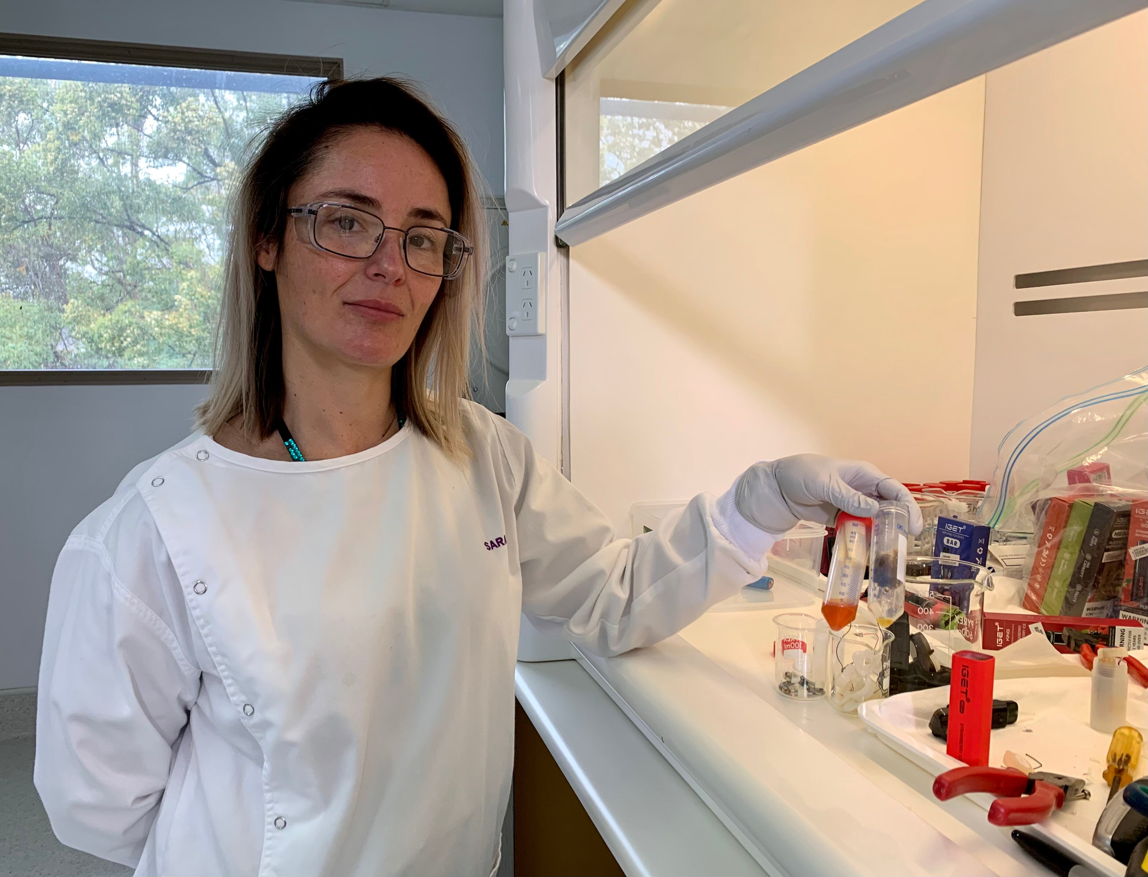 Sarah Mullins is dressed in a lab coat, holding vials at Queensland Health's Forensic and Scientific Services