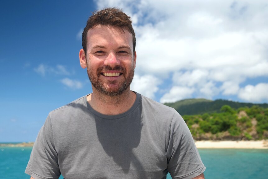 a man sitting on a boat in front of an island smiles at the camera