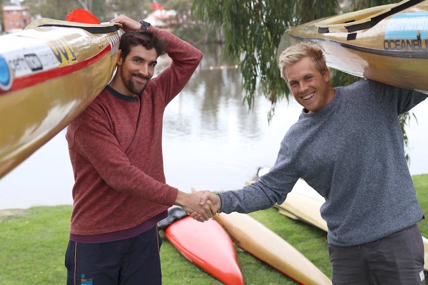 Avon Descent competitors Josh Kippin and Brendan Rice shake hands while holding their kayaks on their shoulders.