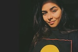 Self portrait of Brooke Blurton, wearing an Aboriginal flag shirt in dark lighting.