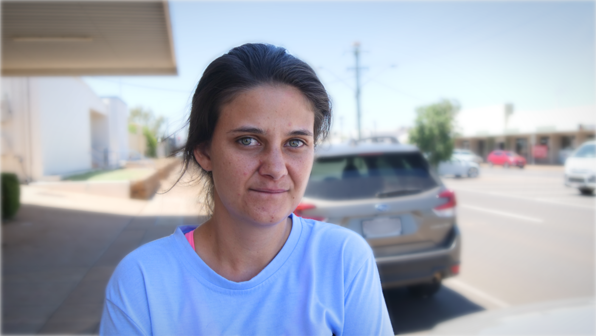 A young woman wearing a blue shirt stares sadly at the camera