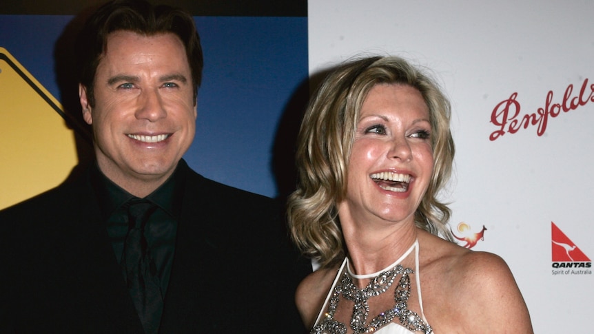 John Travolta and Olivia Newton-John smile while standing on the red carpet